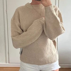 Beige stickad oversized tröja - Supermysig beige stickad tröja med oversized passform och långa ballongärmar. Tröjan har bred ribb vid ärmslut och nederkant samt en enkel rund halsringning. Perfekt för sommarkvällar, höst och vinter!