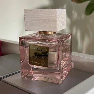 Fleurs de l'Himalaya parfym Rituals - Elegant parfymflaska från Rituals, Fleurs de l'Himalaya. Flaskan är fyrkantig i genomskinligt rosa glas med en stor, vit träliknande kork och en guldig etikett framtill. Perfekt för dig som gillar lyxiga och fräscha dofter.