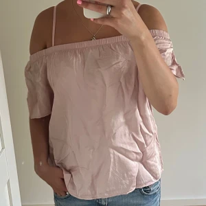 Ljusrosa offshoulder blus - Söt ljusrosa blus med offshoulder och korta ärmar. Toppen har en avslappnad passform och resår upptill som håller den på plats. Perfekt för varma dagar och enkel att styla med jeans eller kjol.