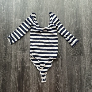 Randig långärmad body i bomull - Snygg body med marinblå och vita ränder, långärmad och med djup rundad urringning. Tillverkad i mjuk bomull som känns skön mot huden. Perfekt att styla med jeans eller kjol för en cool och enkel look.