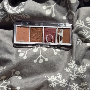 e.l.f. ögonskuggspalett i varma toner - Snygg ögonskuggspalett från e.l.f. med fyra nyanser: matt beige, glittrig koppar, skimrande vinröd och matt brun. Perfekt för att skapa både enkla och mer dramatiska looks. Kompakt plastförpackning med genomskinligt lock.