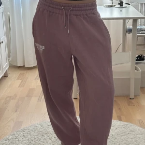 Ljus/smutslila mjukisbyxor från Boohoo S - Säljer ett par ljuslila mjukisbyxor från Boohoo med trycket 'DSGN STUDIO SPORTS CLUB' på benet. Byxorna har elastisk midja med snörning, resår i benslutet, sidofickor och är tillverkade i mjukt bomullsmaterial. 