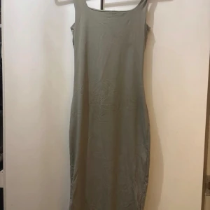 Grå långklänning med smala axelband - En stilren grå långklänning med smala axelband och rundad halsringning. Klänningen har en rak och enkel siluett som ger en clean look. Materialet känns mjukt och stretchigt, perfekt för dig som gillar minimalistisk stil.