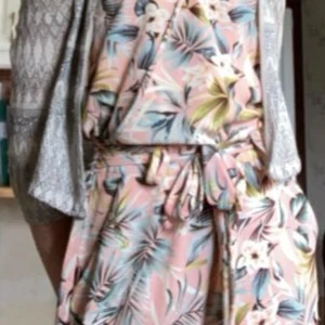 Blommig jumpsuit - Säljer en superfin ärmlös jumpsuit från ONLY i storlek 34. Klänningen har ett tropiskt blommönster i rosa, grönt, vitt och blått, med knytband i midjan och v-ringad hals. 