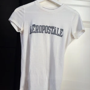 Vit Aeropostale t-shirt  - Vit t-shirt från Aeropostale med mörkblått tryck över bröstet. Klassisk rund halsringning och korta ärmar. 
