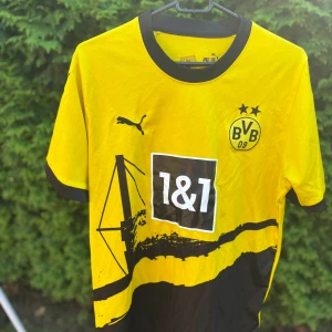 Borussia Dortmund Puma matchtröja gul - Borussia Dortmunds officiella matchtröja från Puma i klassisk gul och svart. Tröjan har korta ärmar, svart krage och detaljer, samt klubbmärke och sponsortryck framtill. Tillverkad i lätt och ventilerande polyester, perfekt för fotboll eller att bära på läktaren. Har ni några frågor är det bara att höra av sig! Pris kan diskuteras 👍