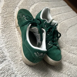 Gröna Adidas Stan Smith sneakers mocka - Snygga gröna Adidas Stan Smith sneakers i mocka med vita detaljer och klassisk logga på hälen.storlek 38.Skorna har snörning, platt sula och rund tå. Perfekta för dig som vill ha en ”everyday” sko. Utmärkt skick på skon. Pris kan diskuteras vidare. 