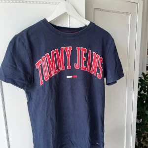 Mörkblå vintage t-shirt Tommy Jeans - Snygg mörkblå t-shirt från Tommy Hillfiger med stort rött och vitt tryck på bröstet. Använd ett fåtal gånger så i ett bra skick!🙌 Storlek S men skulle säga att den även passar en M!