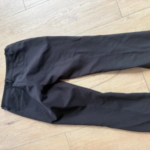 Vera petite kostymbyxor- lågmidjade  - Klassiska svarta kostymbyxor från BikBok i storlek 34. Byxorna har raka ben, hällor för bälte och diskreta bakfickor. Perfekta för en clean och stilren look. Materialet är mjukt och följsamt, vilket gör dem bekväma hela dagen.