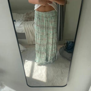 Mintgrön långkjol med mönster - ALDRIG använd, prislapp på.Supersnygg långkjol i mintgrönt med bohemiskt mönster och bred smock i midjan. Kjolen är luftig och har ett flowigt fall, perfekt för dig som gillar avslappnad och cool stil. Färgen är fräsch och detaljerna gör den unik.