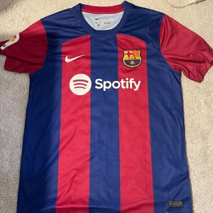 FC Barcelona Lewandowski matchtröja Nike - Säljer en officiell FC Barcelona fotbollströja från Nike med Lewandowski och nummer 9 på ryggen. Tröjan har klassiska blå och röda vertikala ränder, korta ärmar och klubbmärke på bröstet. Materialet är lätt och andas, perfekt för match eller träning.