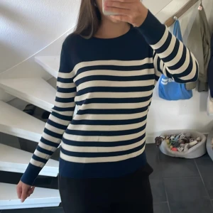 Randig vit-blå merino tröja i storlek S - Snygg randig tröja från Magasin du Nord i marinblått och vitt, tillverkad i 100% fin merinoull. Tröjan har lång ärm, rund hals och tre guldknappar på axeln som cool detalj. Perfekt att styla till jeans eller kostymbyxor en höst dag 🍂