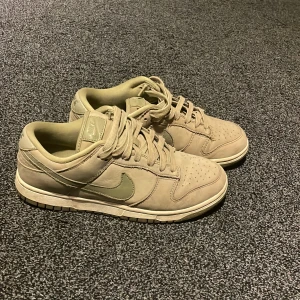 Nike Dunk Low i grön mocka - Nike Dunk Low sneakers i oliv grön mocka med ljusgröna swoosh-detaljer. Klassisk siluett med rund tå, snörning och platt sula. Perfekta för dig som gillar stilrena och neutrala färger med en twist. Snygga till både jeans och cargo pants. Köptes nya i Nike butiken för 1399kr säljes nu för 500kr