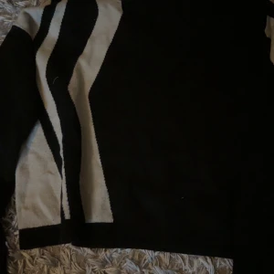 Svart och beige stickad tröja Object - Säljer en stickad tröja från Object i svart och beige med coolt vågigt mönster. Tröjan har lång ärm och en lite loose passform, perfekt för dig som gillar en stilren men ändå unik look.