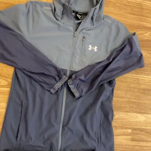 Blå träningsbyxor från Under Armour -  Endast träff!!Snygga marinblå träningsbyxor från Under Armour med resår i midjan och vid bensluten. Byxorna har en diskret logga på låret och är gjorda i ett lätt och smidigt syntetmaterial som passar perfekt för träning. Fickor med dragkedja på sidorna.