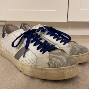 Vita sneakers från D.A.T.E. med blå glitter - Unika vita sneakers från D.A.T.E. med hexagonmönstrad skinnstruktur, silverfärgad mesh framtill och blå glittriga detaljer på hälen. Skorna har blå glittriga snören och en grå rand på sidan. Perfekt för dig som vill sticka ut med coola detaljer.