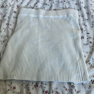 Vit ribbad kjol från Gina Tricot - Säljer en vit ribbad kortkjol från Gina Tricot. Kjolen är stickad med breda vertikala ränder och har en mjuk, stretchig midja. Materialet består av 84% akryl och 16% polyamid, vilket gör den både bekväm och lätt att bära. Perfekt för dig som gillar enkel och clean stil.