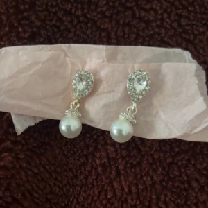 Glittriga örhängen med pärlor - Snygga örhängen med droppformad, glittrig topp i silverfärg och hängande vita pärlor. Perfekt för dig som vill ha en elegant och lyxig vibe. De gnistrar fint och har en klassisk design som verkligen sticker ut.