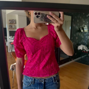 Rosa blus med puffärm och broderi - Superfin rosa blus med korta puffärmar och v-ringning. Blusen har broderade detaljer och ett genombrutet mönster som ger en unik look. Perfekt till jeans eller kjol för en färgstark outfit.