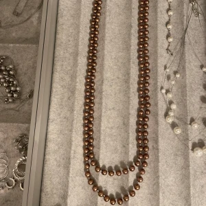 Pärlhalsband vintage - Halsbandet är långt men kan dubblas till två lager för kortare. Pärlorna är runda brunfärgade och har en glansig yta. 