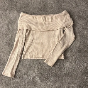 Beige offshoulder topp Gina Tricot - Superfin ribbad offshoulder topp från Gina Tricot i beige. Långärmad och croppad modell med bred krage som sitter snyggt över axlarna. Perfekt för dig som gillar en stilren och trendig look.