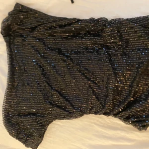 Svart glittrig kortklänning med paljetter - Säljer en svart blus från monki som är täckt av glittriga paljetter. Blusen har en snygg, figurnära passform och är perfekt för dig som vill sticka ut med lite extra bling. Materialet är mjukt och följsamt, och har en festlig vibe.