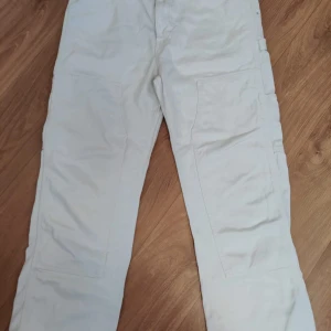Vita cargopants med raka ben - Säljer ett par vita cargopants med raka ben och stora sidofickor. Byxorna har en clean look och är perfekta för dig som gillar streetstyle. Materialet känns som bomull och de har en avslappnad passform. Passar dig som vill ha en enkel men snygg stil.