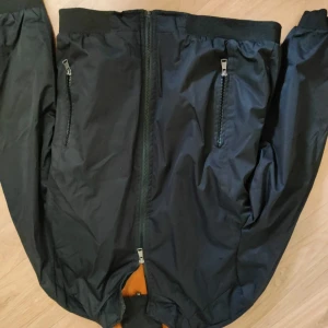 Svart bomberjacka med dragkedjor - Snygg svart bomberjacka med två dragkedjefickor framtill och ribbade muddar vid ärmslut och midja. Jackan har hel dragkedja och en orange detalj på insidan. Perfekt för dig som vill ha en stilren och enkel look.