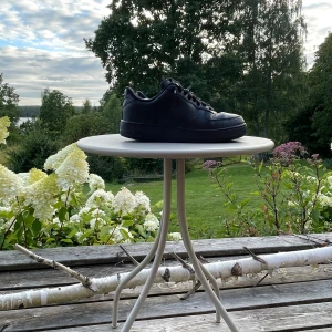 Svarta Nike Air Force 1 sneakers - Klassiska helsvarta Nike Air Force 1 sneakers i skinn med rund tå och snörning. Snygg och tidlös modell med perforerade detaljer på tån och robust platt sula. Perfekta för dig som gillar streetstyle och vill ha en ikonisk sneaker i garderoben.
