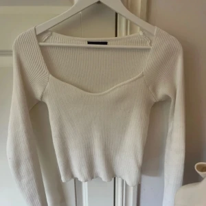 Vit ribbad långärmad topp - Snygg vit ribbad topp med lång ärm och v-ringad halsringning. Modellen är croppad och har en figurnära passform som framhäver siluetten. Perfekt att styla med jeans eller kjol för en trendig look.