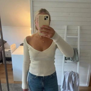 Vit ribbad offshoulder tröja - Säljer en vit ribbad tröja med offshoulder och v-ringad hals. Tröjan har lång ärm och sitter snyggt figurnära. Materialet är stretchigt och mjukt, perfekt för dig som gillar en clean och stilren look. Passar till jeans eller kjol för en trendig vibe.