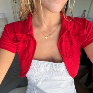 Röd croppad jacka från OXYD - Snygg röd bolero från OXYD med korta ärmar och coola fickdetaljer framtill. Jackan har klassisk krage och är gjord i mjukt, stretchigt material som sitter skönt. Perfekt för att lyfta vilken outfit som helst med en poppig färg.