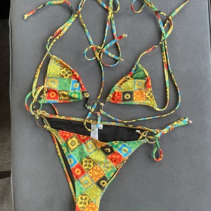 Färgglad bikini från NA-KD - Snygg och färgglad bikini från NA-KD med ett unikt mönster i gult, rött, blått och grönt. Bikinin har knytband och dekorativa ringdetaljer. Perfekt för sommarens stranddagar!