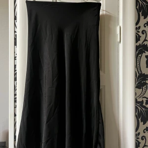 Svart satinkjol från New yorker - Säljer en svart kjol från Amisu i storlek 34 flowy siluett med lätt utställd nederdel. Materialet känns slätt och har ett snyggt fall. Perfekt för dig som gillar minimalistisk och stilren look.