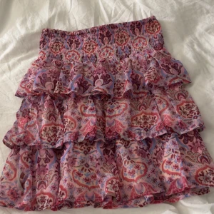 Volangkjol med mönster från Lindex - Säljer en superfin kort volangkjol från Lindex med färgglatt mönster i rosa, storleken är 170 men passar mig som brukar ha m/s i kjolar