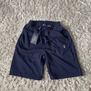 Marinblå shorts från Polo Ralph Lauren - Snygga marinblå shorts från Polo Ralph Lauren med klassisk logga broderad på benet. De har elastisk midja med snörning och är tillverkade i mjuk bomull, perfekta för en chill och sportig stil.