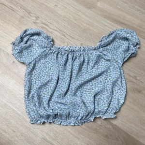 Blommig offshoulder blus från Friends - Supersöt blommig offshoulder blus från Friends i ljusblått med små vita och gula blommor. Modellen är croppad med resår i både halsringning och nederkant samt puffiga korta ärmar. Perfekt för sommarens alla tillfällen!