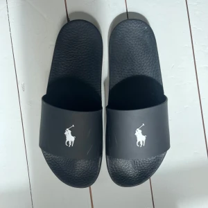 Tofflor Polo Ralph Lauren - Badtofflor från märket Polo Ralph Lauren. De har endast blivit använda någon gång. De har några repor på ovansidan, se bilder. Annars är de i mycket bra skick! Skokartongen på den sista bilden medföljer. Nypris 999kr