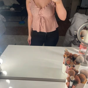 Söt volangtop från SHEIN i rosa och vit  - Volangig topp från SHEIN i ljusrosa med broderade hålmönster och knyt framtill. Axelbandslös känsla med smala axelband och volangkant vid urringningen. Croppad modell som ger en luftig och somrig vibe, perfekt till höga jeans eller kjol.