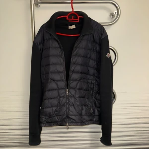 Moncler Cardigan  - Säljer äkta Moncler Maglione Tricot Cardigan strl L. Dunpanel fram, stickade ärmar/rygg. Nypris ca 850–950 €. Begagnad med slitage: liten reva fram, slitna muddar med hål, mindre sömslitage. Alla dragkedjor ok, ingen lukt. Rök- & djurfritt hem. Endast kofta, utan dustbag/kvitto. Pris: 2000kr
