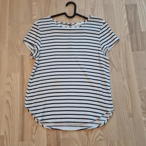 Vit och svart randig blus - Snygg H&M blus med svarta horisontella ränder på vit botten. Rund halsringning och korta ärmar ger en chill vibe. Baksidan har en liten öppning med knapp. Perfekt till jeans eller kjol för en enkel, fräsch look.