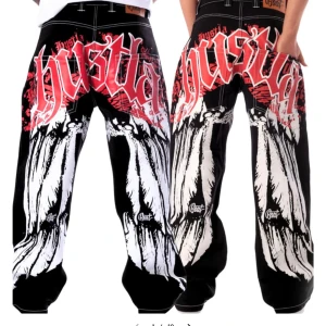 Svarta wide jeans med graffiti-tryck - Riktigt feta svarta jeans från BSAT med bred passform och kontrastsömmar. Baksidan har stort graffiti-inspirerat tryck i rött och vitt med texten 'hustla' och coola grafiska detaljer längs benen. Perfekta för dig som vill sticka ut och köra streetstyle vibes. De har små imperfektioner vid hälen och säljs därför för 950 istället för 1223. Skriv för bilder. Säljer då de blivit lite för små och sällan kommer till användning.