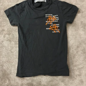 Svart Off-White t-shirt med broderi - Svart t-shirt från Off-White med coolt tryck och orange broderade figurer på bröstet. Text i vitt och detaljerad design från Virgil Abloh. Klassisk rund hals och korta ärmar, tillverkad i mjuk bomull. Perfekt för dig som gillar streetwear och unika plagg. Tvättas innan köp!