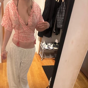 Rosa och vit omlottopp med snörning - Säljer en superfin omlottopp i rosa och vitt med grafiskt mönster. Toppen har djup v ringning, korta ärmar och snörning med tofsar i midjan. Croppad modell som sitter snyggt och är perfekt för varma dagar. Sitter fast med en hårsnodd där bak då den är lite stor men med säkretsnålar kan du fixa den lite hur du vill. Storlek M, använt sparsam. 