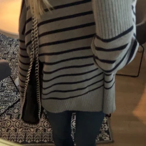 Grå randig stickad tröja från Zara - Säljer en chill grå stickad tröja från Zara med mörkblå horisontella ränder. Tröjan har loose passform, bred ribbad kant nedtill och vid ärmslut, samt långa ärmar. Perfekt att slänga på sig till jeans för en avslappnad look.