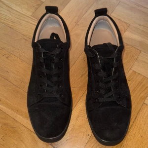 Christian Louboutin Mocha sneakers - Stilrena svarta sneakers från Christian Louboutin i mjuk mocka med klassisk röd sula och diskret logga. Skorna har rund tå, svarta skosnören och en låg profil som passar till allt. Insidan är i ljust skinn för extra komfort och lyxig känsla.