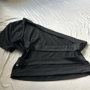 Svart oneshoulder topp från SHEIN - Svart oneshoulder topp från SHEIN i stretchigt material. Toppen har en kort ärm på ena sidan och är avskuren på andra axeln för en cool asymmetrisk look. Tillverkad i mjuk polyesterblandning som sitter snyggt och bekvämt.