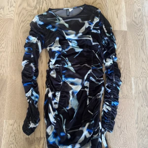 Mönstrad meshklänning från H&M Divided - Säljer en tight kortklänning från H&M Divided med coolt abstrakt mönster i svart, blått och vitt. Klänningen har långa ärmar, rynkade detaljer längs sidorna och är gjord i tunn mesh med stretch. Perfekt för dig som vill sticka ut!