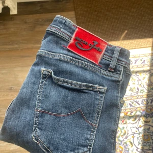 Jacob Cohën jeans med röd detalj - Snygga blå jeans från Jacob Cohën, modell Style 622 (Den populäraste). Jeansen har röda kontrastsömmar, röd patch med logga bak och broderad J på myntfickan. Klassisk femficksmodell med knappgylf och raka ben. Tillverkade i mjukt denimtyg.