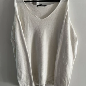 Vit stickad tröja från 157, v-ringad - En vit stickad tröja från 157 med v-ringad hals och långa ärmar. Tröjan har en loose passform och ribbade muddar vid ärmslut och nederkant. Perfekt för lager-på-lager och chill vibes. Använd men i mycket bra skick